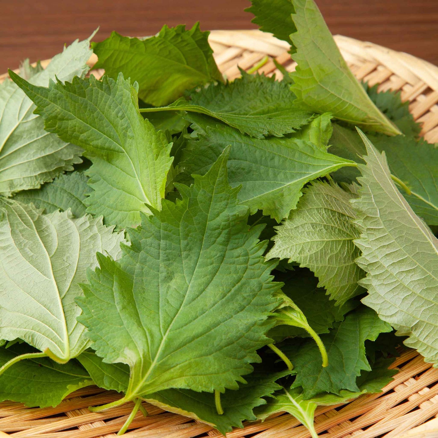 Fresh perilla leaves on a woven basket with a wooden background