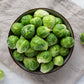 A bowl of several green Dagan F1 brussels sprouts showing layered leaves on a neutral cloth