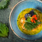 Dish with yellow sauce, salmon, and perilla garnishes on a blue plate