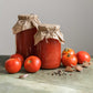 Two jars of tomato sauce with a bow, surrounded by fresh ace 55 tomatoes and garlic on a wooden surface.